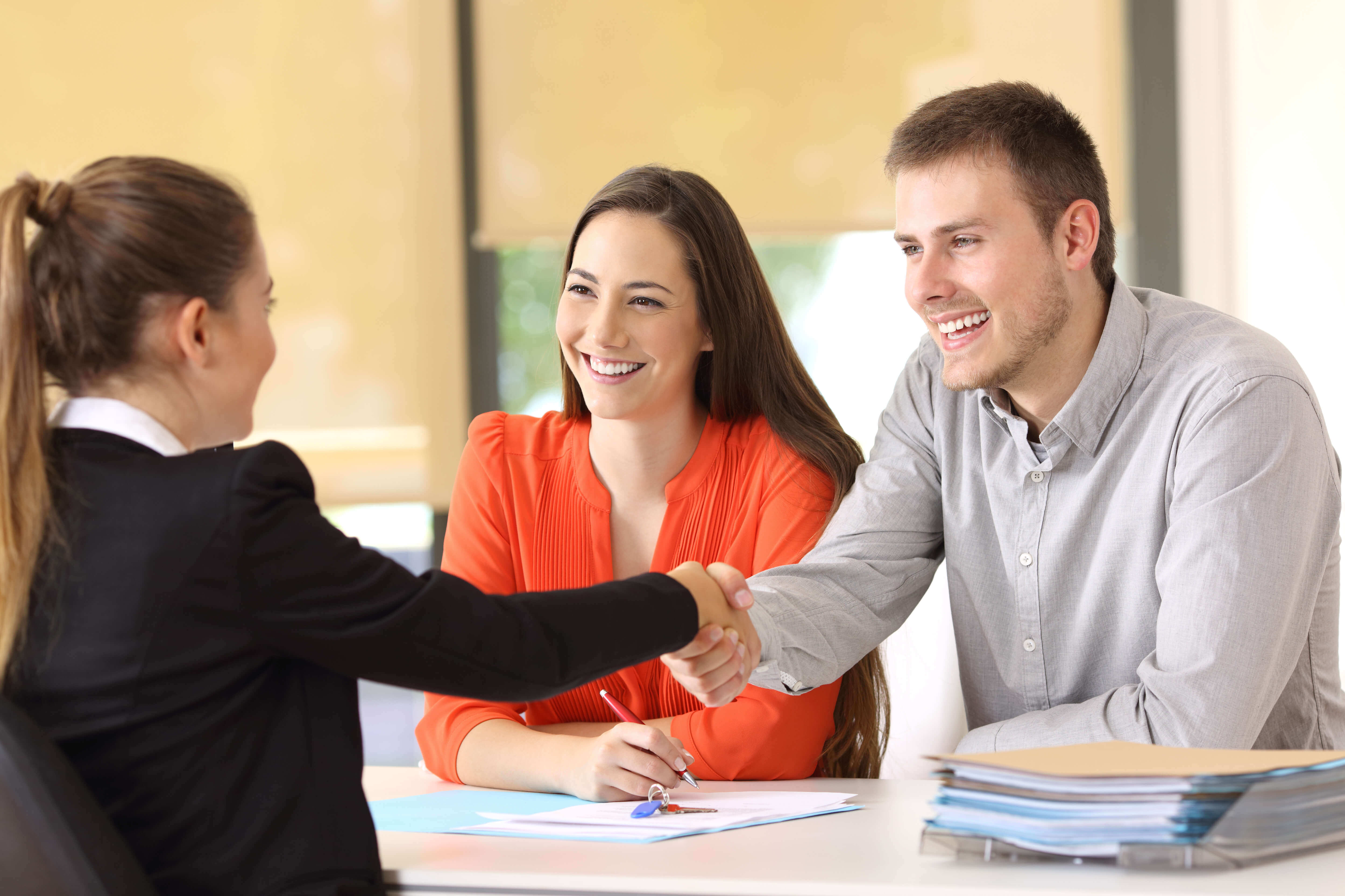 Smiling couple shaking agents hand at a real estate closing